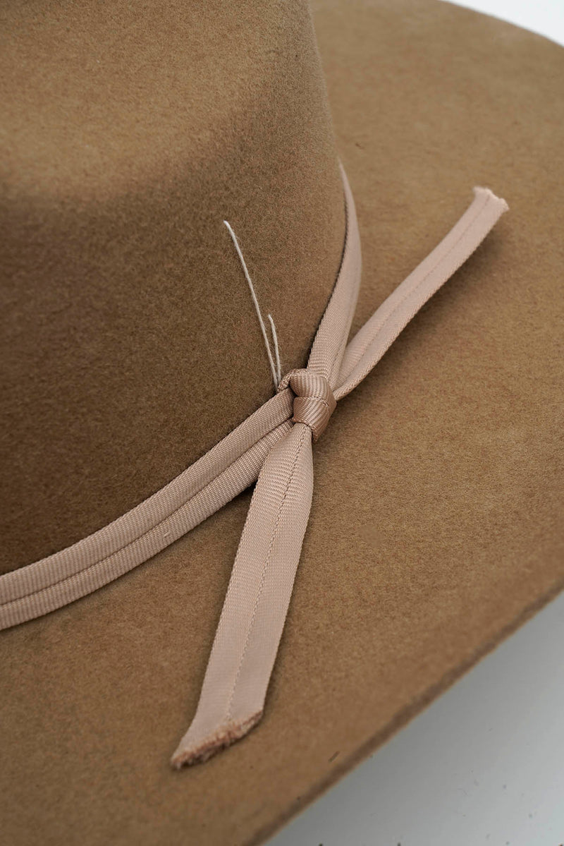 Tan cowboy felt hat with a ribbon on a white background